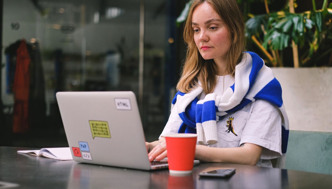 A journalist writing at a laptop in a cafe