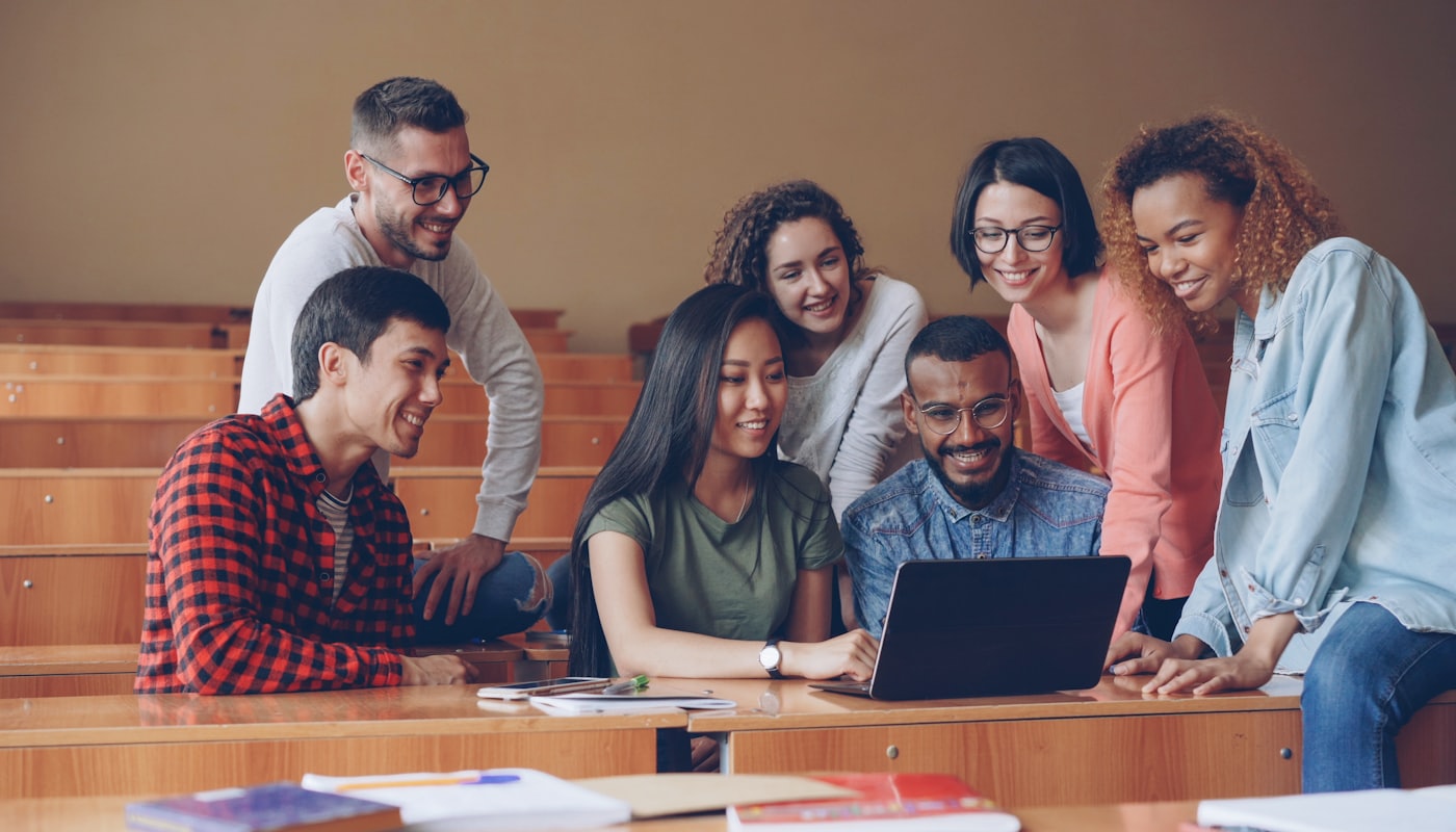 A diverse group of students gathered around a laptop together in class