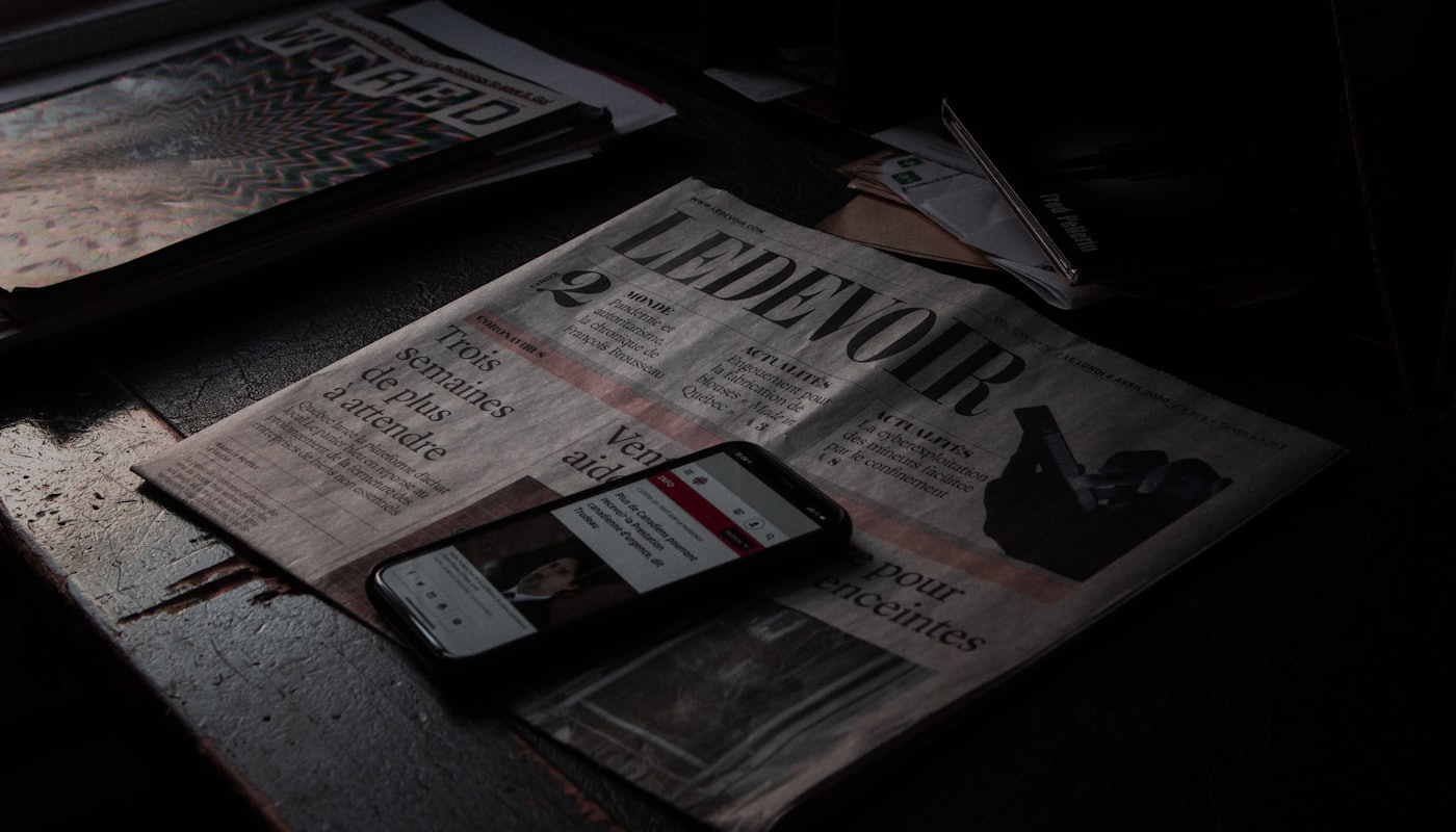 A smartphone showing a news app resting on a folded newspaper