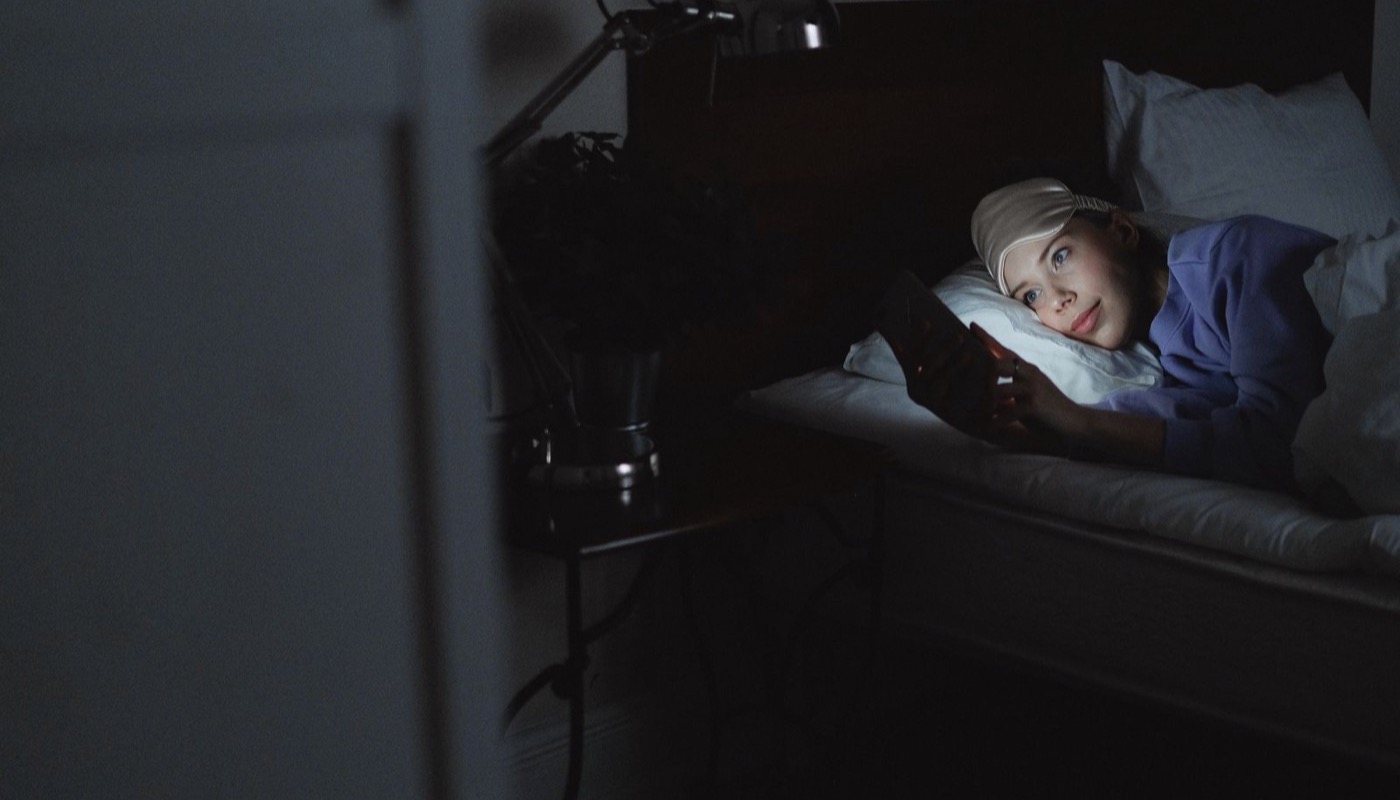 A person lying in bed at night looking at a phone