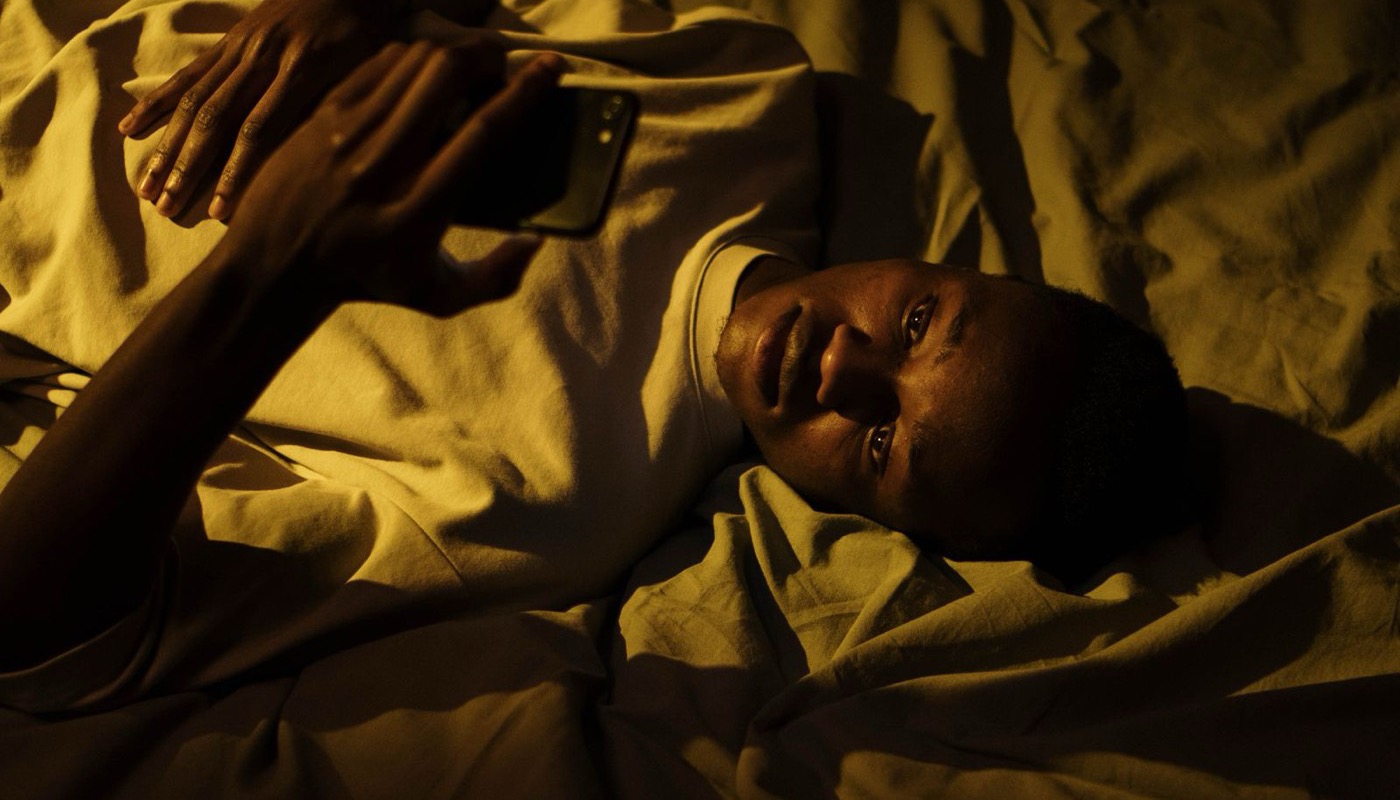 A person lying in a dark room, face lit by a phone screen