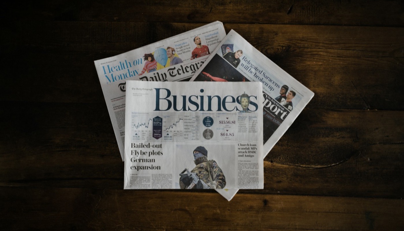 Several newspapers fanned out on a wooden table