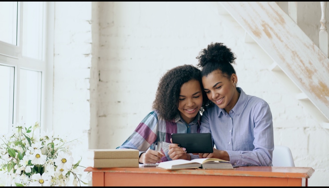 Two students learning together with a tablet and books