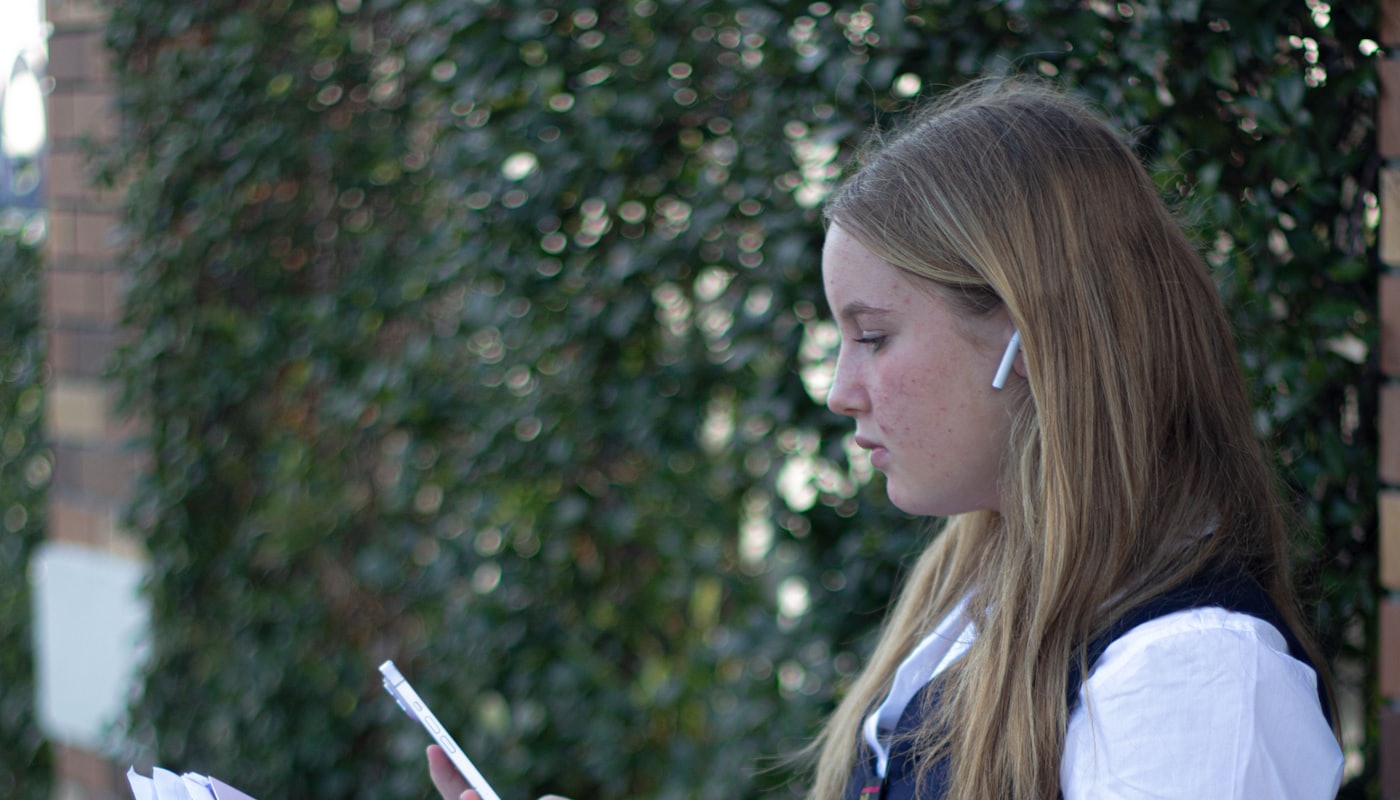 A high school student in uniform reading the news on her phone outside