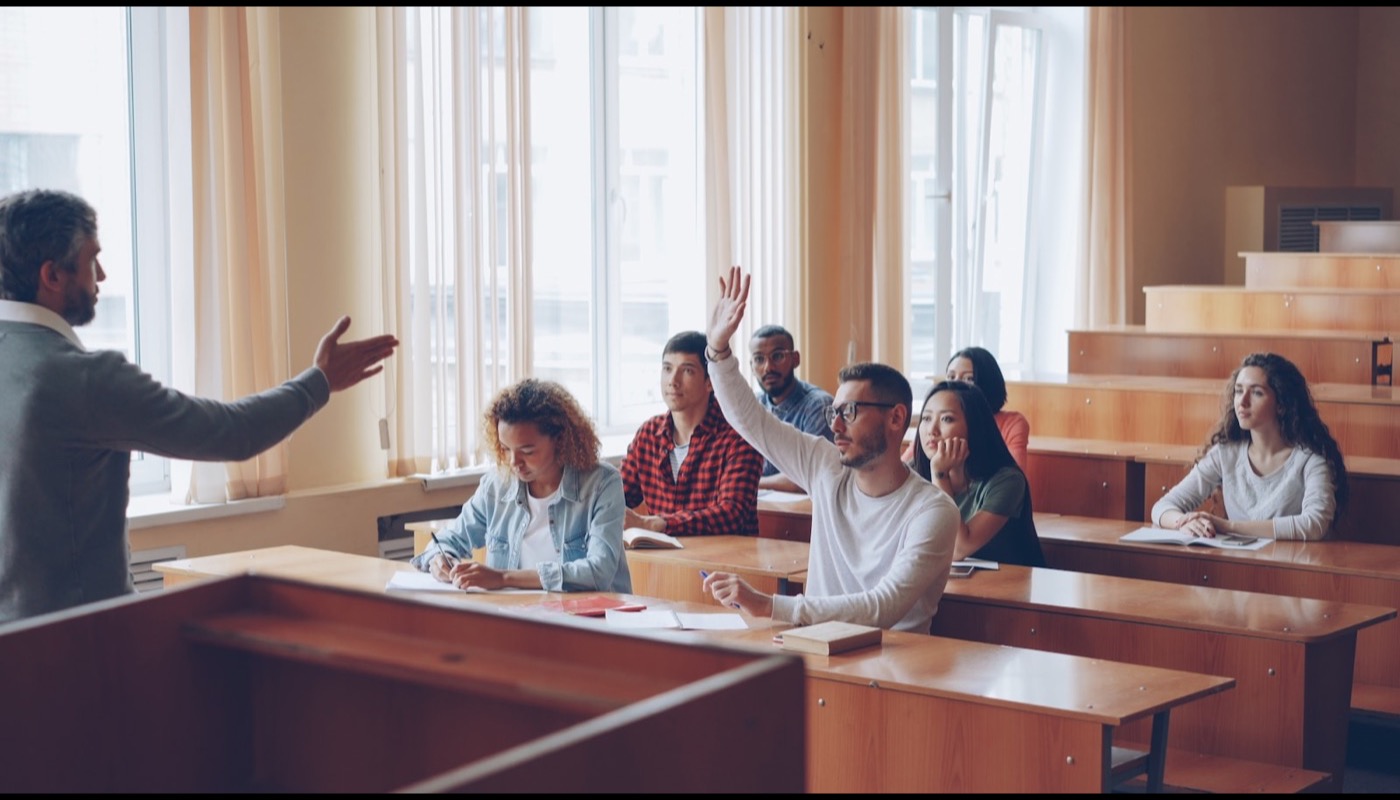 A student raising a hand in class as the teacher gestures